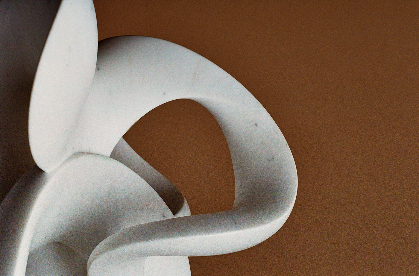 Close up abstract white marble sculpture looping around itself in front of a brown background