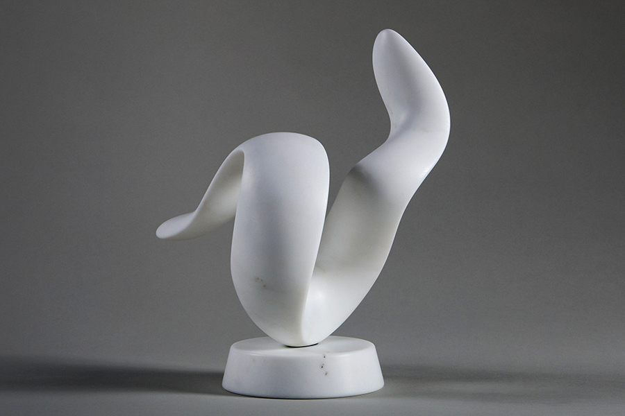 white abstract sculpture on a white base sits in front of grey background