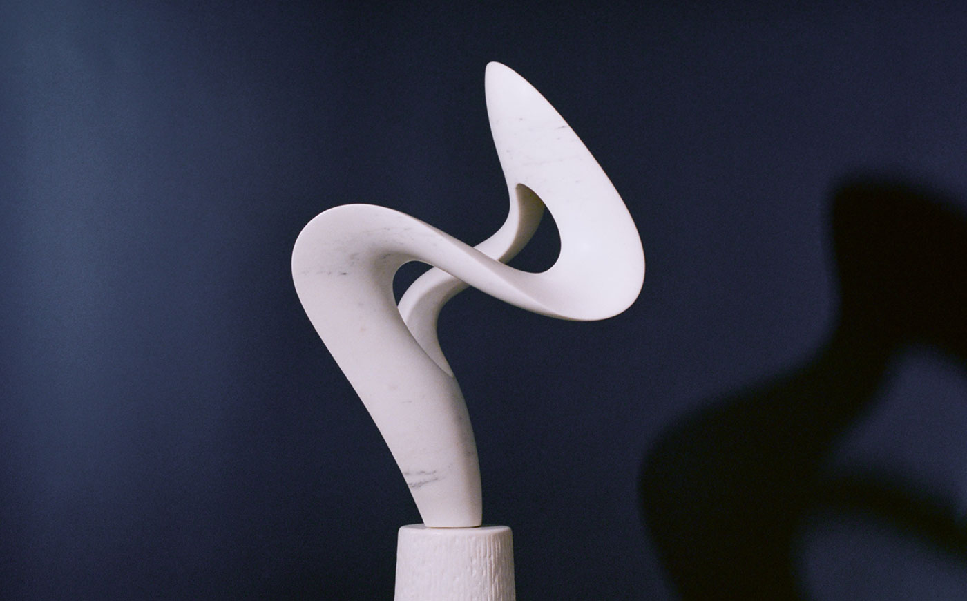 Abstract marble sculpture, white with graceful curves in front of blue background