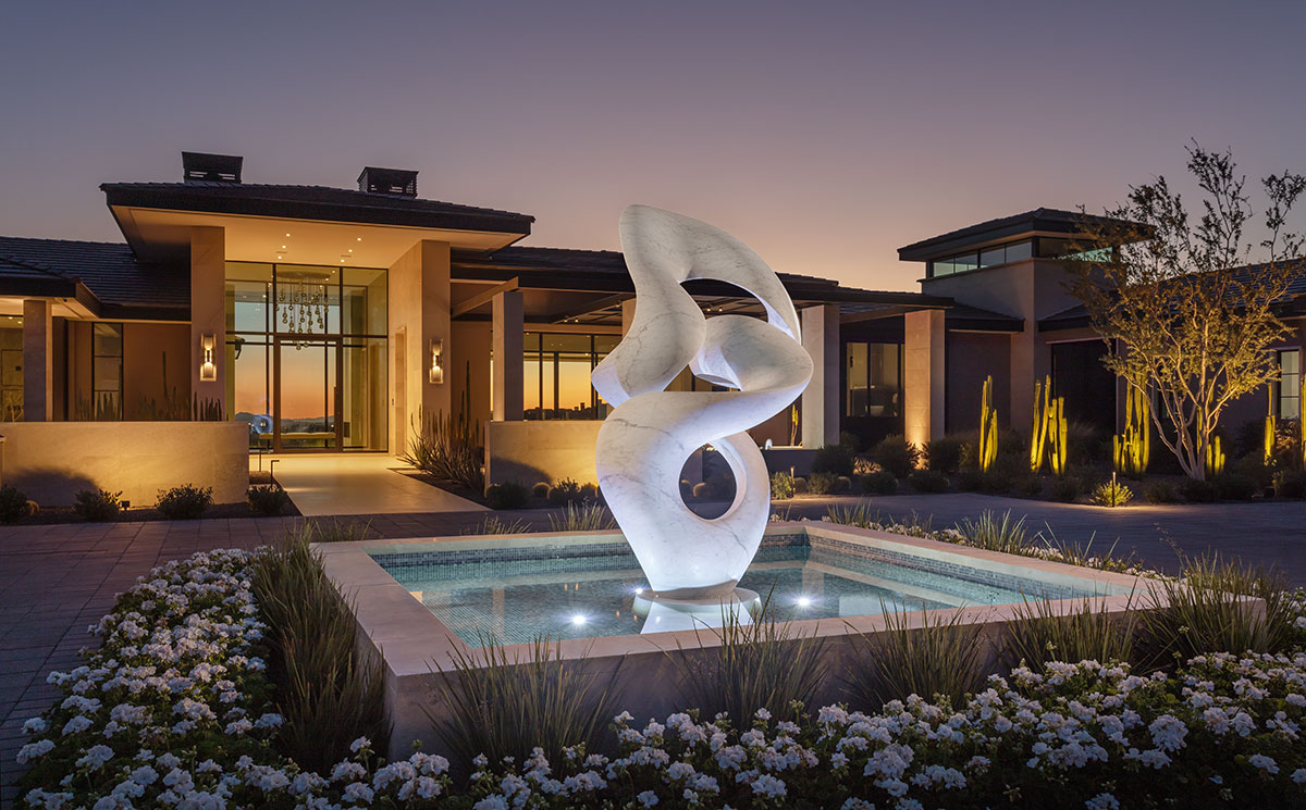 a monumental white marble sculpture sited on a reflecting pool with a opulent desert home at dusk in the background